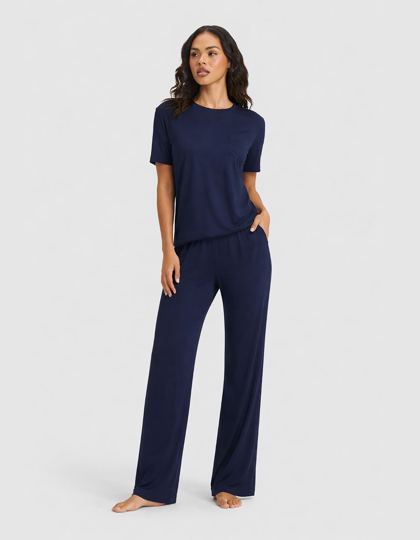 A woman stands barefoot in the Cozy Earth Women's Bamboo Stretch-Knit Lounge Tee & Pant Set—a matching short-sleeve top and wide-leg pant—posing against a plain light gray background.
