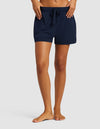 A person stands barefoot in Cozy Earth's Women's Bamboo Stretch-Knit Shorts, navy blue with a drawstring, and a matching top, hands resting on the waistband against a plain light background.|Color:Navy