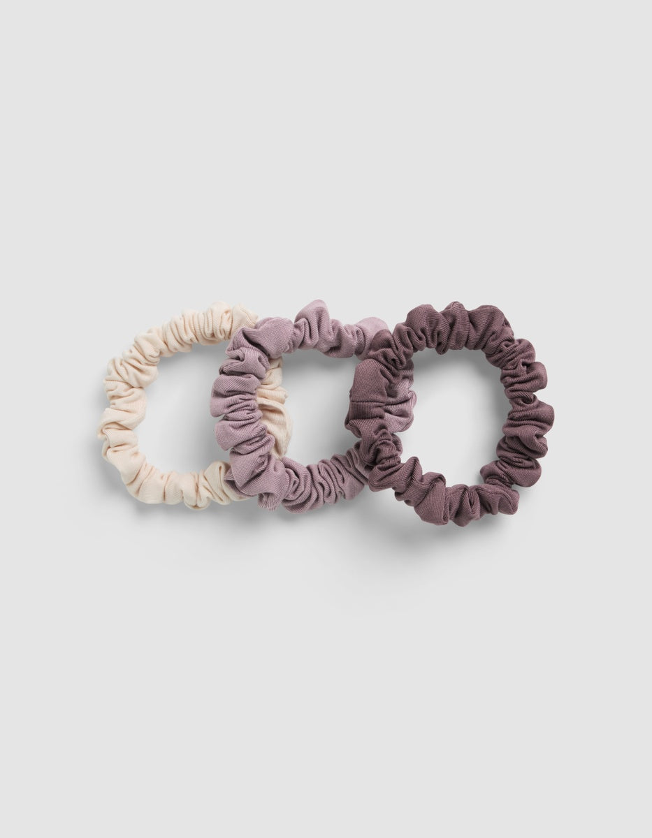 Three Cozy Earth Bamboo Stretch Knit Skinny Scrunchies in cream, mauve, and dark purple arranged in a row.