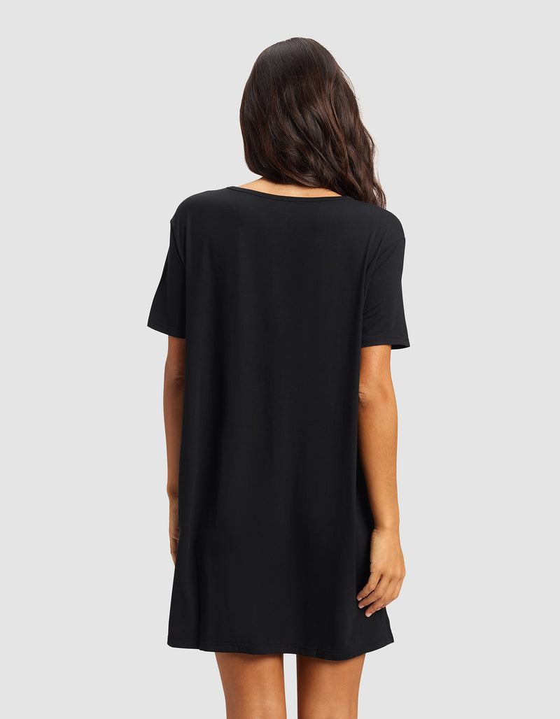 A woman with long, wavy dark hair is shown from the back, wearing the Cozy Earth Women's Bamboo Stretch-Knit Sleep Dress in black against a plain light gray background.