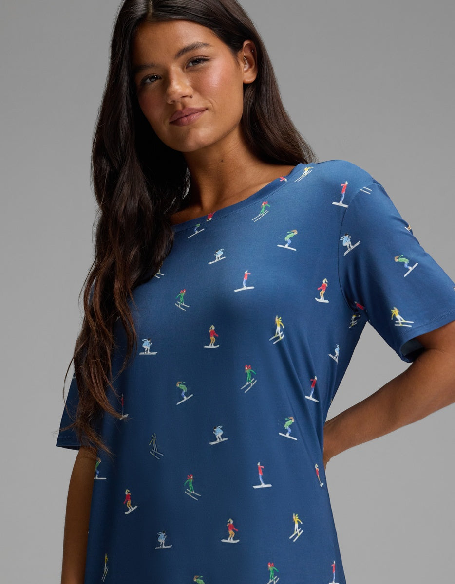 A person wearing a blue Cozy Earth Women’s Bamboo Stretch-Knit Sleep Dress with a pattern of small figures skiing.