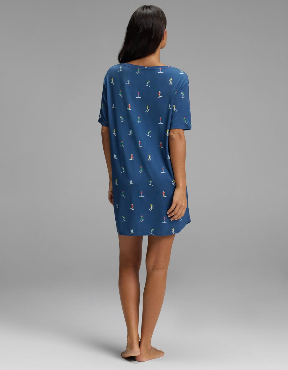 A person seen from behind wearing a blue short-sleeved Cozy Earth Women’s Bamboo Stretch-Knit Sleep Dress featuring a colorful pattern of small skiers.