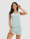 A woman with long dark hair wears the Cozy Earth Women's Bamboo Stretch-Knit Lounge Tank in light blue, smiling and touching her hair as she stands against a plain light background.|Color:Brook