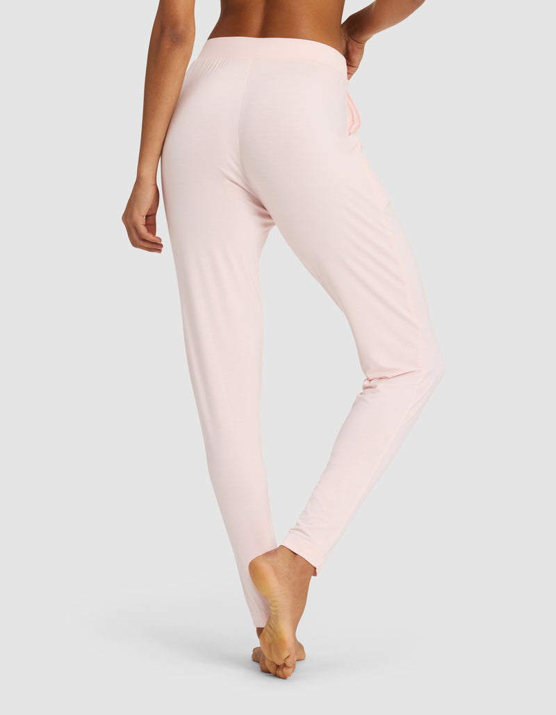 A person stands barefoot on tiptoe, shown from the waist down in a light setting, wearing Cozy Earth Women's Bamboo Stretch-Knit Tapered Pant in light pink.