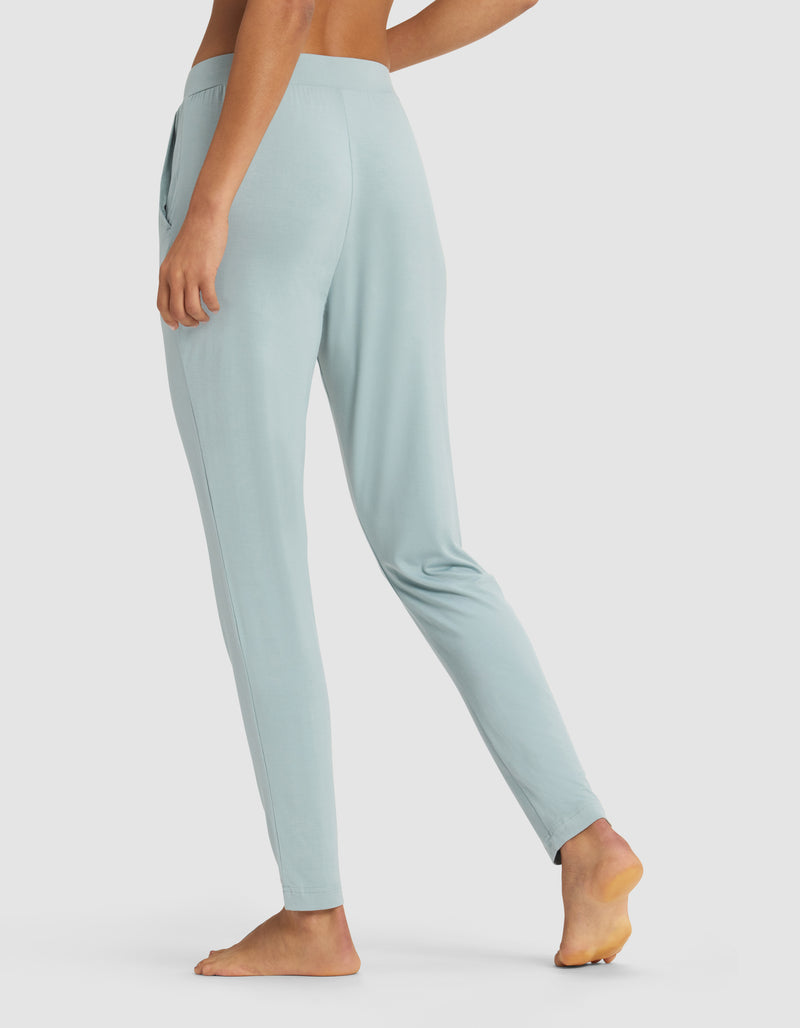 A person stands barefoot on tiptoe, wearing Cozy Earth’s Women’s Bamboo Stretch-Knit Tapered Pant in light blue, shown from the back and side. The high-waisted, slim-fit jogger is displayed against a plain background with the image cropped from the upper chest down.