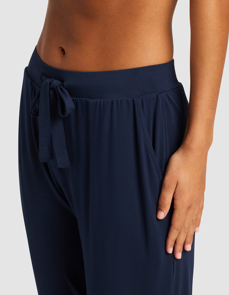 A woman wears Cozy Earth's Women's Bamboo Stretch-Knit Tapered Pant in navy blue, posing from waist to mid-thigh with her right hand in the pocket against a plain background.