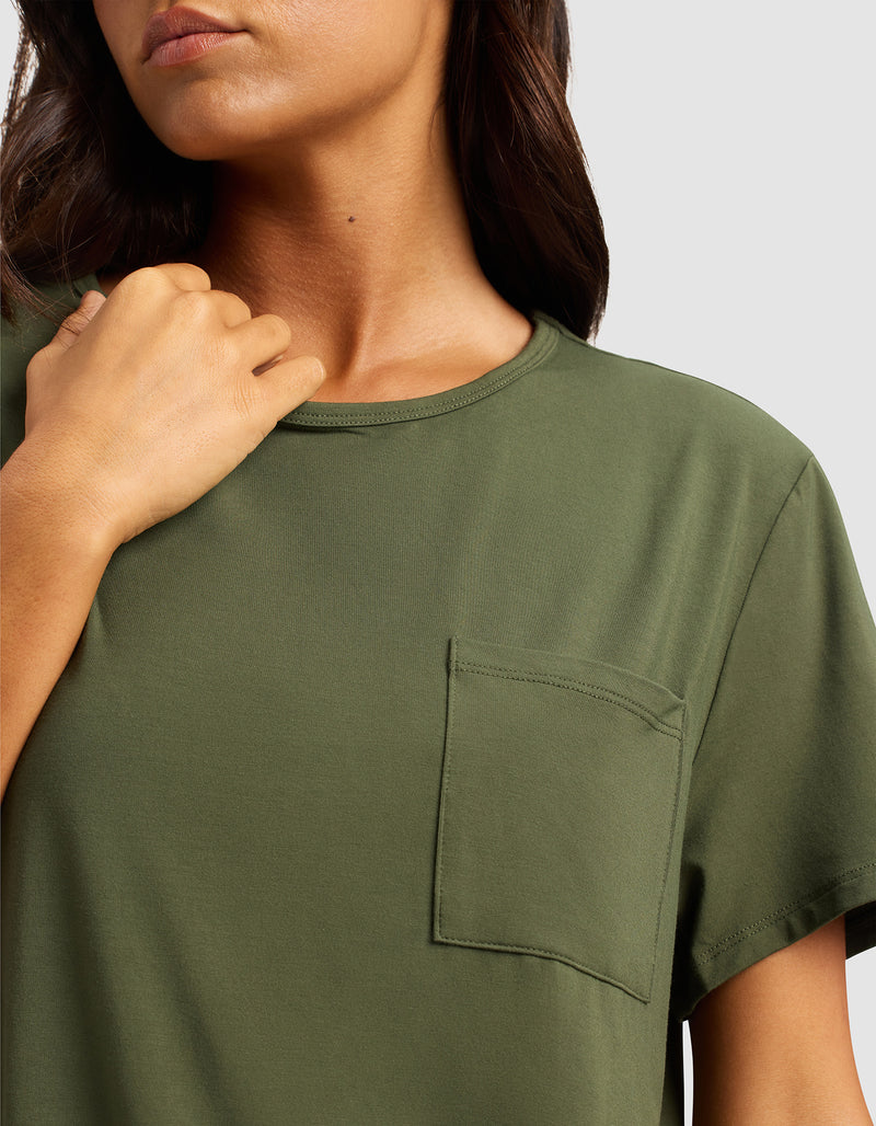 A woman models the Cozy Earth Women's Bamboo Stretch-Knit Lounge Tee in olive green, featuring short sleeves and a chest pocket, with one hand near her collarbone against a plain light gray background.