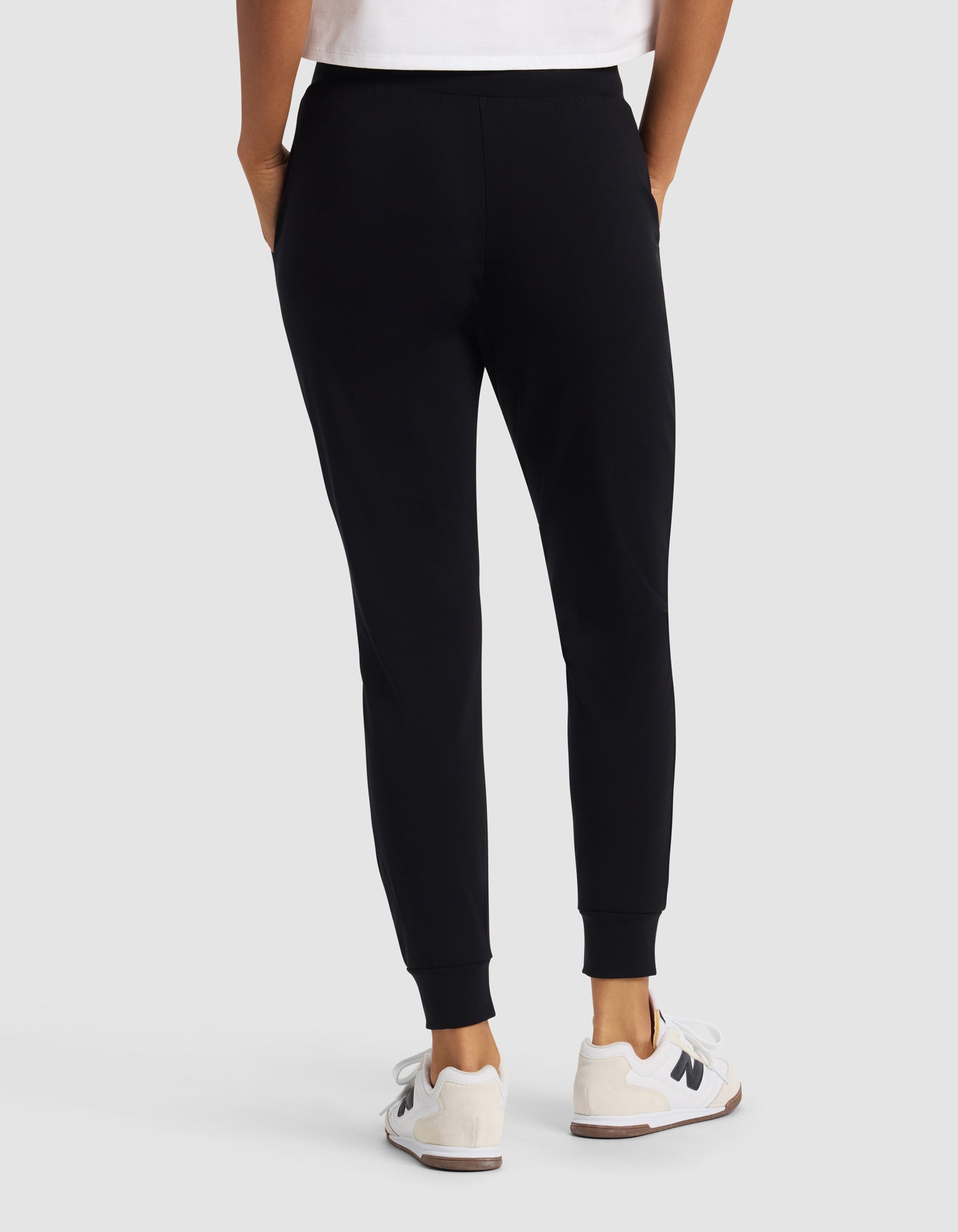 A woman is shown from the back wearing Cozy Earth’s Women's Brushed Bamboo Jogger Pant in black, paired with white sneakers featuring a black "N" logo and a partially visible white shirt, set against a plain light background.