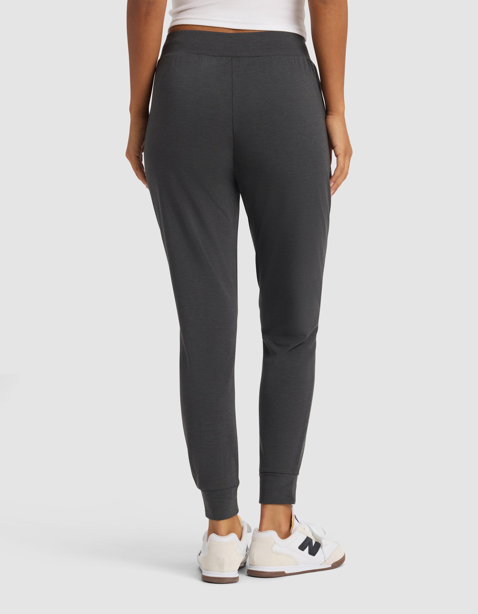 A person is shown from behind against a plain background, wearing a white top, white New Balance sneakers, and dark gray Cozy Earth Women's Brushed Bamboo Jogger Pants.