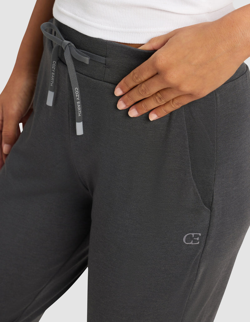 A person wearing the Cozy Earth Women's Brushed Bamboo Jogger Pant in dark gray, featuring side pockets and a small "CE" logo by the left pocket, pairs it with a white top and rests a hand on their hip.