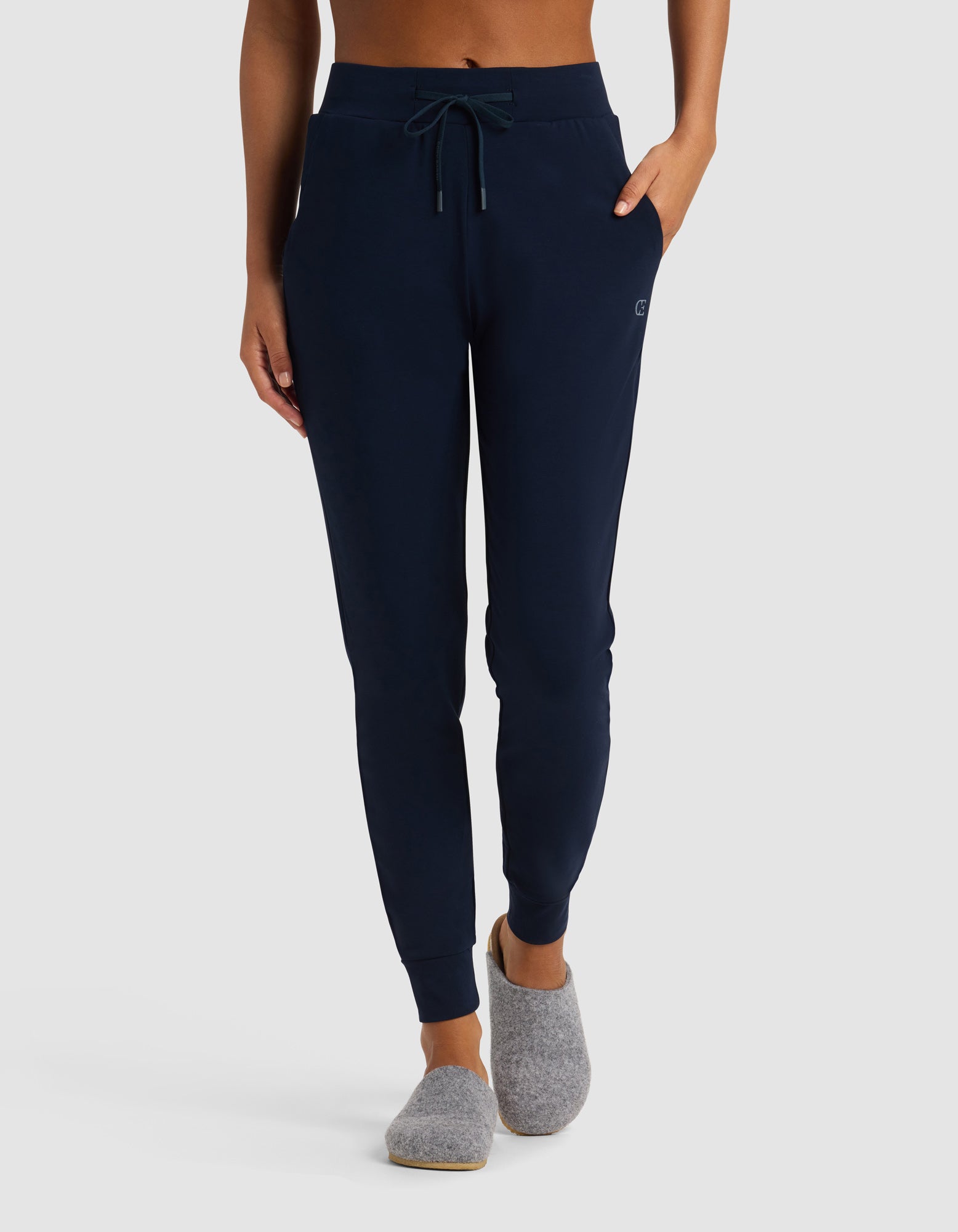 A person stands against a plain light background wearing Cozy Earth Women's Brushed Bamboo Jogger Pant in navy blue with a drawstring waist and gray slippers; their upper body is not fully visible.