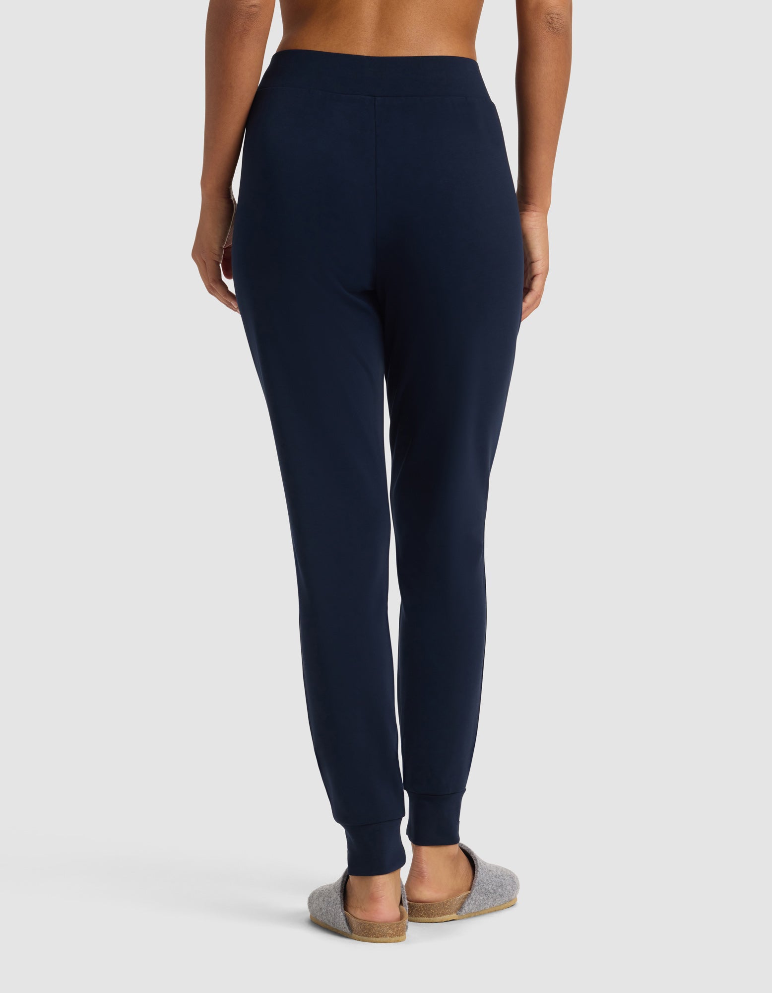 A person is seen from the back wearing Cozy Earth’s Women's Brushed Bamboo Jogger Pant in navy blue with gray slippers, standing against a plain light background.