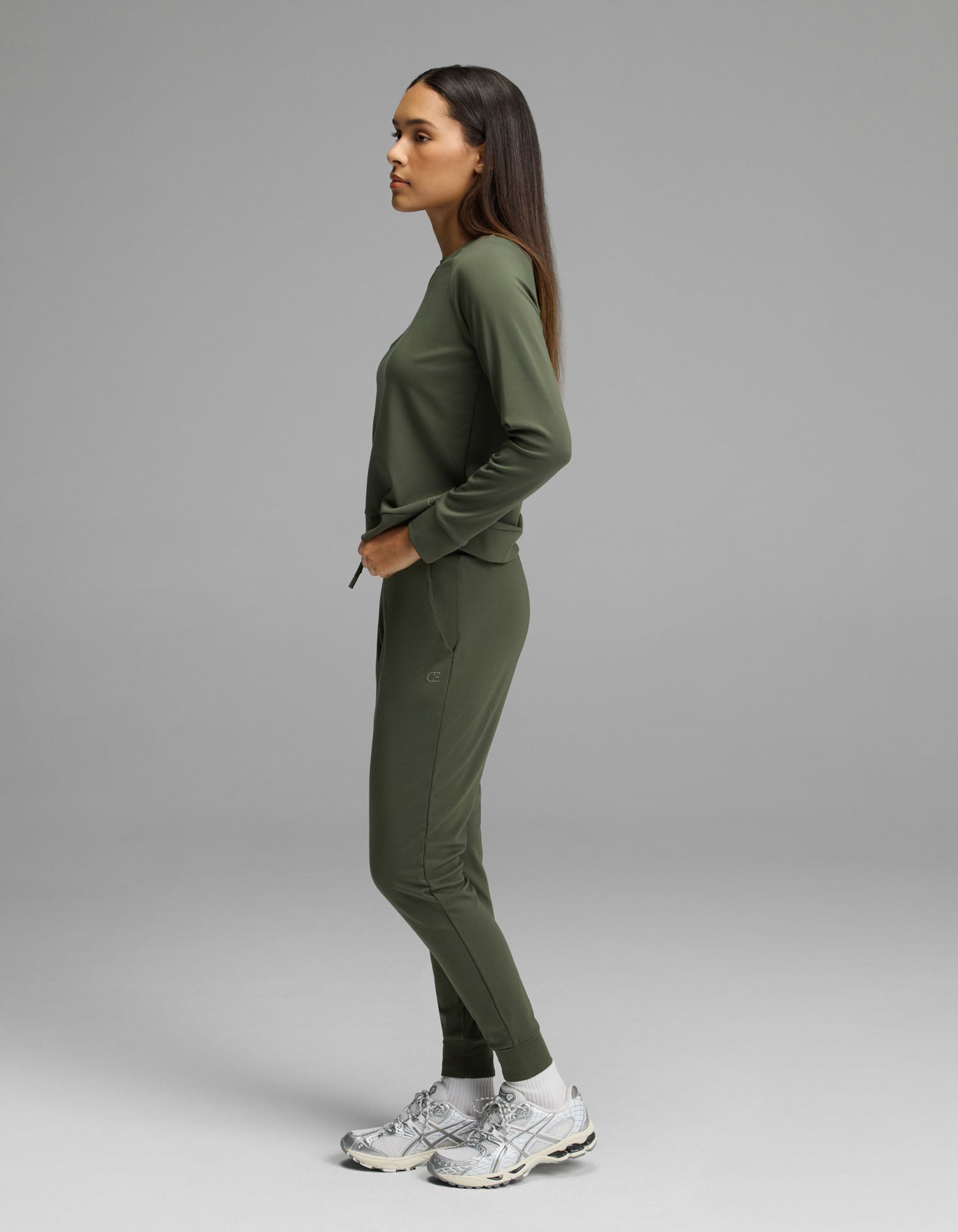 A person stands in profile against a plain background, wearing the Women’s Brushed Bamboo Jogger Set by Cozy Earth with white sneakers.
