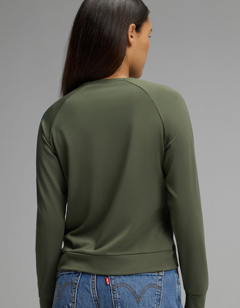 A person with long brown hair is shown from the back, wearing the Cozy Earth Women’s Brushed Bamboo Pullover Crew in olive green and blue jeans against a plain gray background.