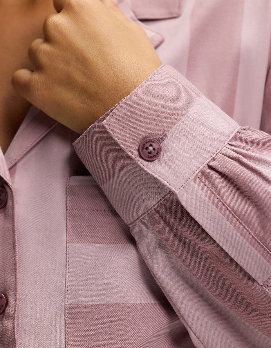 A close-up of a person’s hand adjusting the cuff of the Cozy Earth Women’s Belmont Long Sleeve Pajama Top in mauve, featuring pleated sleeve details and a single cuff button.
