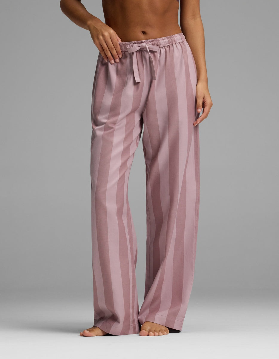 A person stands barefoot wearing Cozy Earth’s Women’s Belmont Pajama Pant, featuring a loose fit, pink color, vertical stripes, and a drawstring waist. The upper body is mostly out of frame.|Color:Viola Stripe