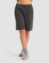 A person wearing Cozy Earth Women's Brushed Bamboo Bermuda Shorts in dark gray and light gray socks stands with legs crossed against a plain light background. The top half of their body is not visible.|Color:Charcoal