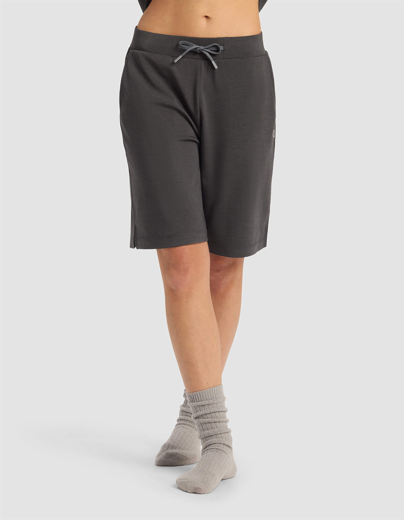A person wearing Cozy Earth Women's Brushed Bamboo Bermuda Shorts in dark gray and light gray socks stands with legs crossed against a plain light background. The top half of their body is not visible.