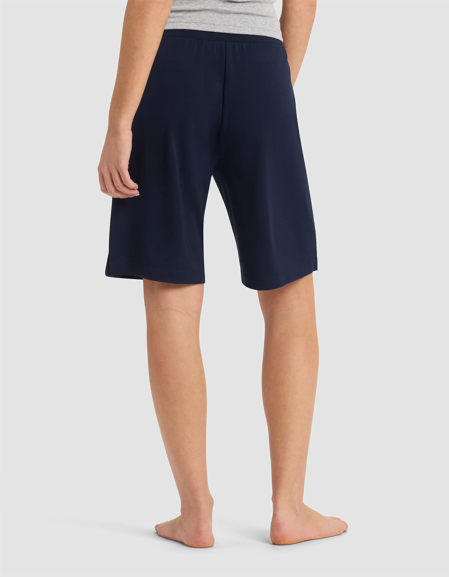 A person stands barefoot, shown from the back, wearing a gray top and Cozy Earth's Women's Brushed Bamboo Bermuda Shorts in navy blue that reach just above the knees.