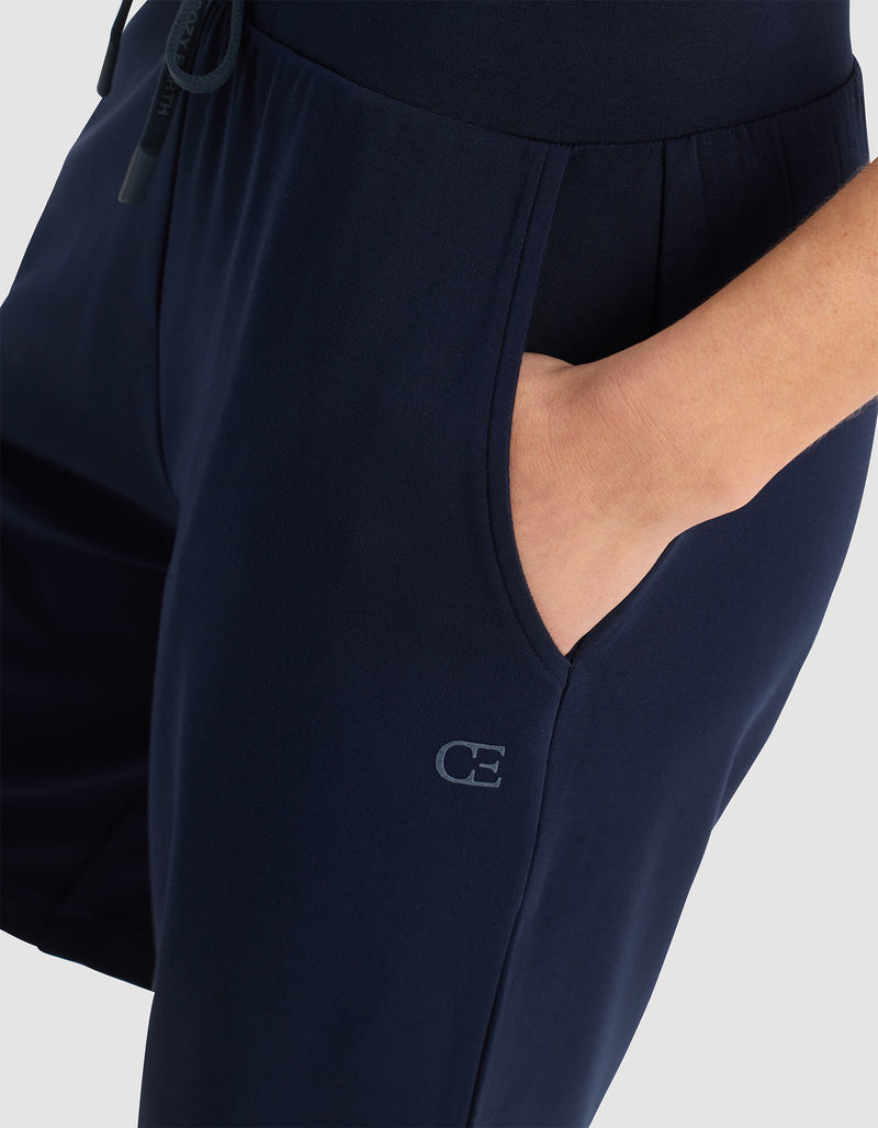 A person wears Cozy Earth Women's Brushed Bamboo Bermuda Shorts with a hand in the pocket. The shorts are navy blue and have a small "CE" logo near the pocket, set against a plain, light-colored background.
