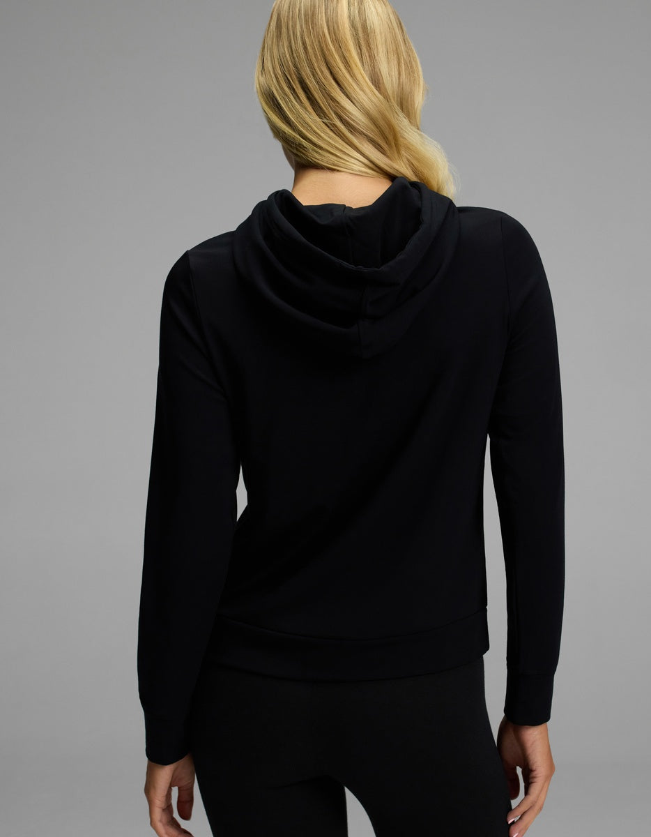 A woman with long blonde hair, seen from behind, is wearing the Cozy Earth Women’s Brushed Bamboo Hoodie and black pants against a plain gray background.