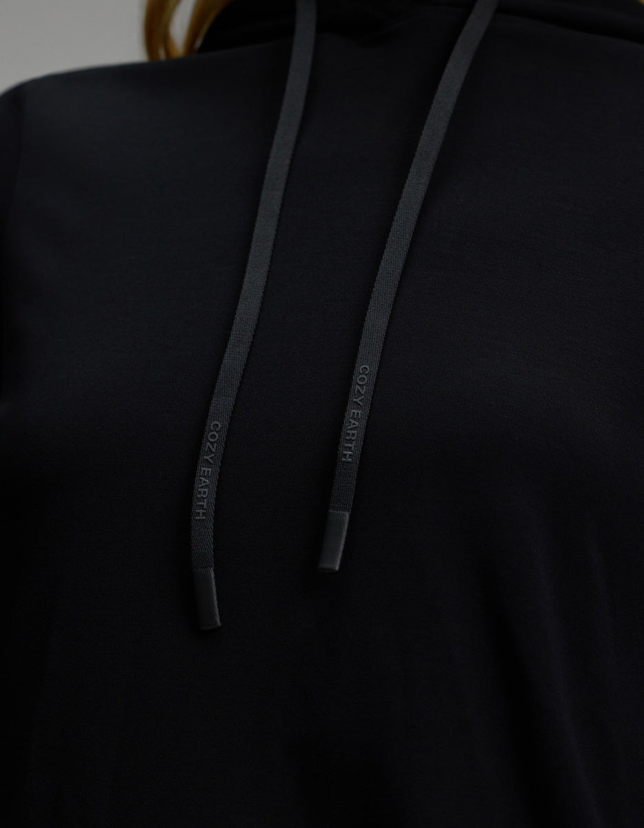 Close-up of the Women’s Brushed Bamboo Hoodie by Cozy Earth in black, highlighting the chest area and two black drawstrings with “COZY EARTH” embossed on the tips.
