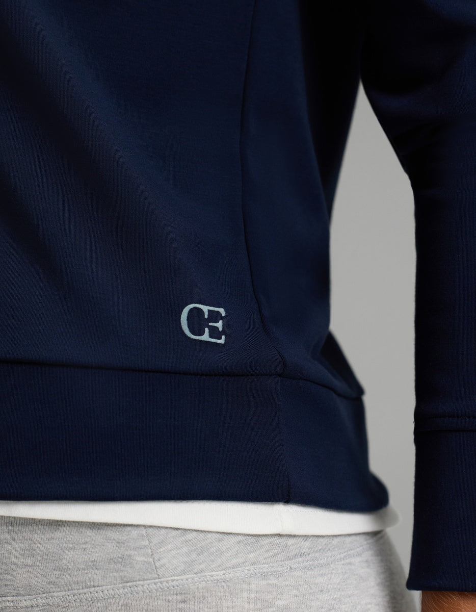 Close-up of a person wearing the Cozy Earth Women’s Brushed Bamboo Hoodie in navy blue with a small “CE” logo near the hem, layered over a white shirt and paired with light gray pants.