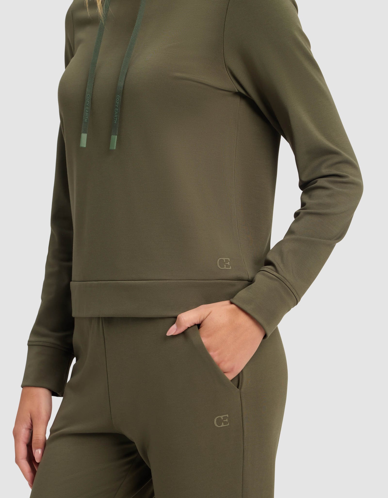 A woman models the Cozy Earth Women's Brushed Bamboo Hoodie in olive green, paired with matching pants, standing against a plain background with one hand in her pocket.