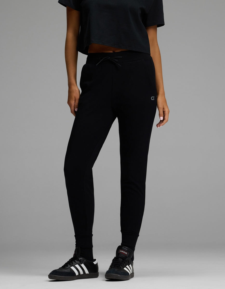 A person wearing the Cozy Earth Women’s Brushed Bamboo Jogger in black, along with a black cropped t-shirt and black Adidas sneakers, stands against a plain gray background. Their face is not visible.|Color:Black