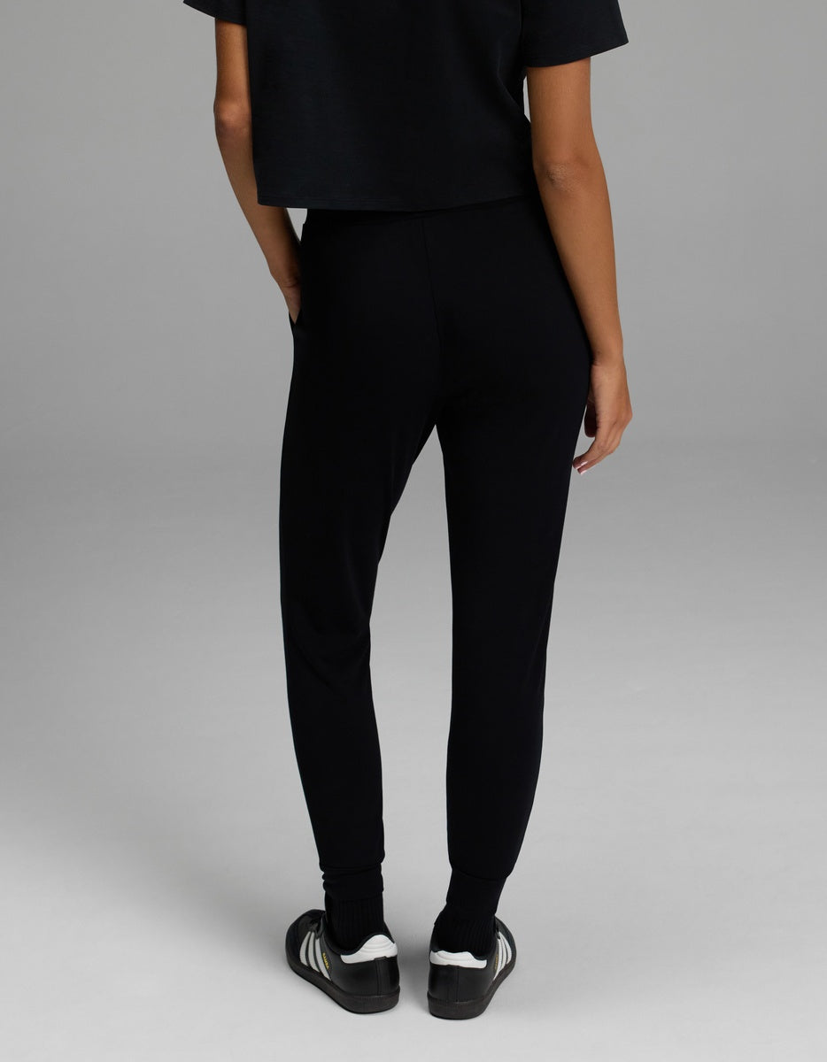 Shown from the back and standing against a gray background, a person is pictured wearing the Cozy Earth Women’s Brushed Bamboo Jogger in black. Only the lower half of the body is visible.
