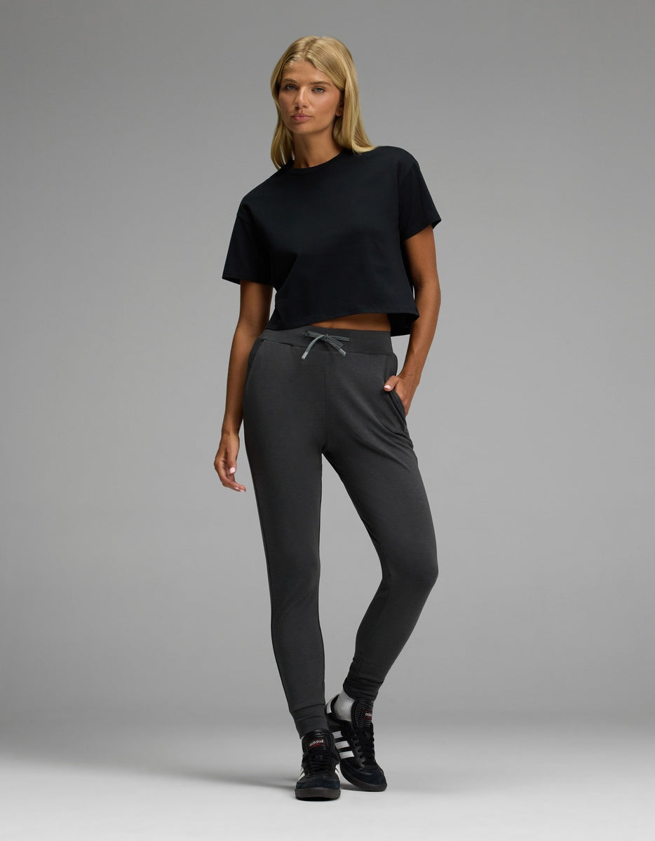 A woman poses in Cozy Earth’s Women’s Brushed Bamboo Jogger and a black crop t-shirt paired with black sneakers against a plain gray background.