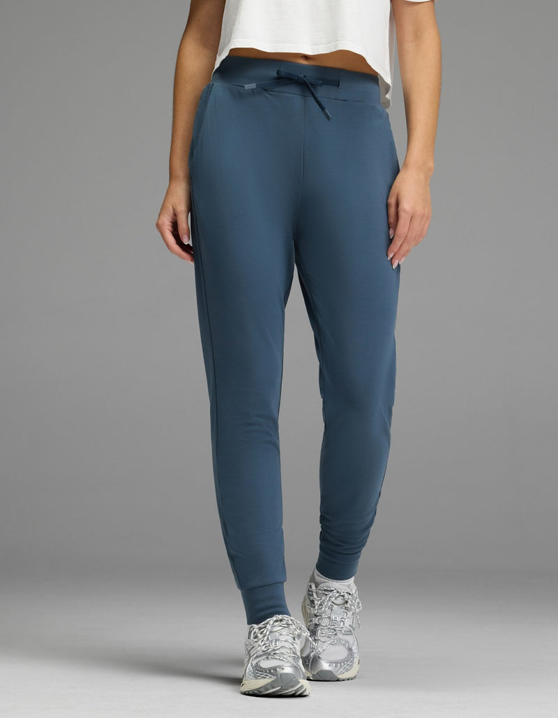 A person stands against a plain gray background wearing the Cozy Earth Women’s Brushed Bamboo Jogger in Dawn, paired with a white cropped shirt and gray athletic shoes.
