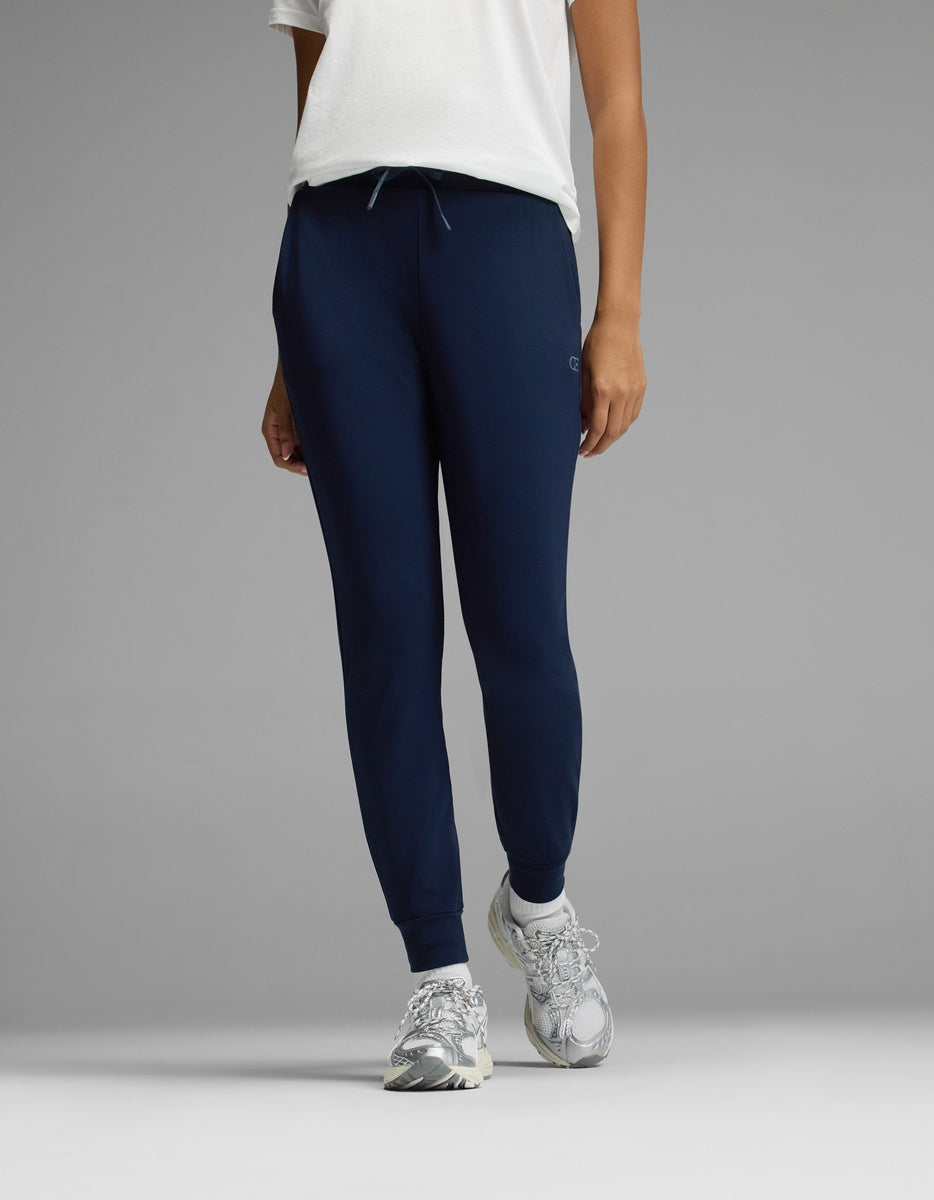 Person wearing a white t-shirt, Cozy Earth Women’s Brushed Bamboo Jogger in navy, and white sneakers, standing against a plain gray background. The image is cropped at the shoulders.