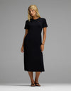 A woman wearing the Cozy Earth Women’s Brushed Bamboo Midi Dress in black, paired with black sandals, stands against a plain grey background.|Color:Black