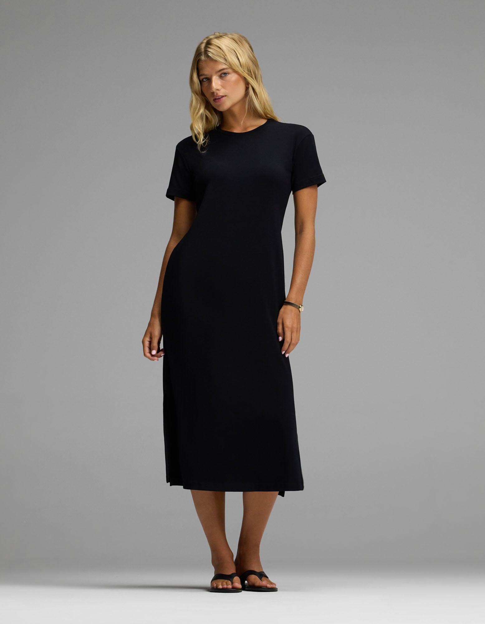 A woman wearing the Cozy Earth Women’s Brushed Bamboo Midi Dress in black, paired with black sandals, stands against a plain grey background.|Color:Black