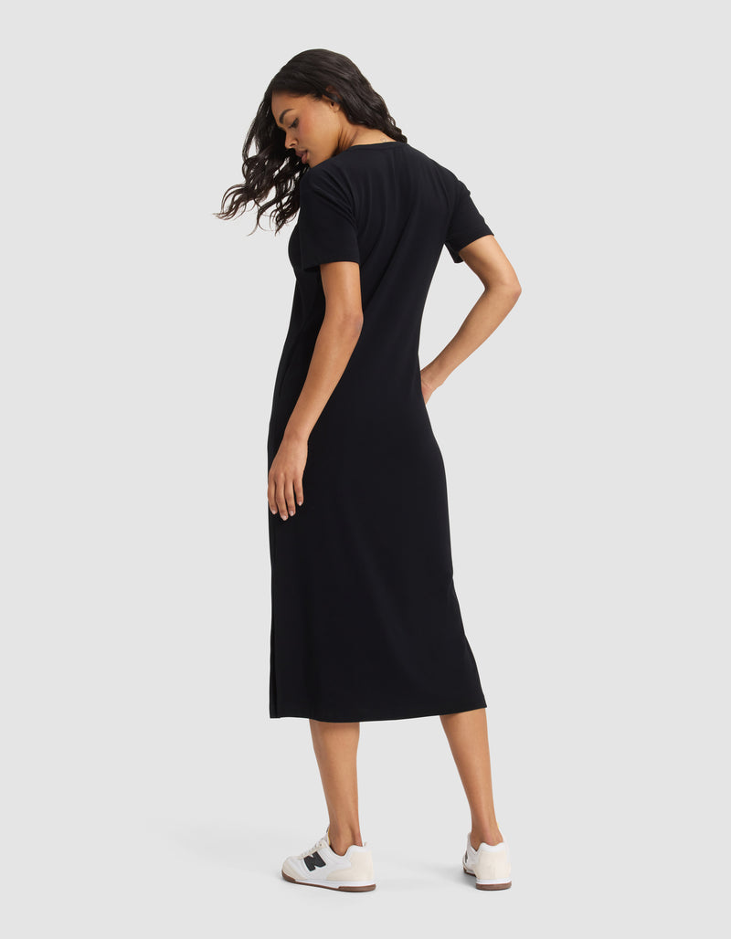 A woman faces away, head turned left, modeling the Cozy Earth Women's Brushed Bamboo Midi Dress in black with short sleeves and white sneakers, set against a plain light background.