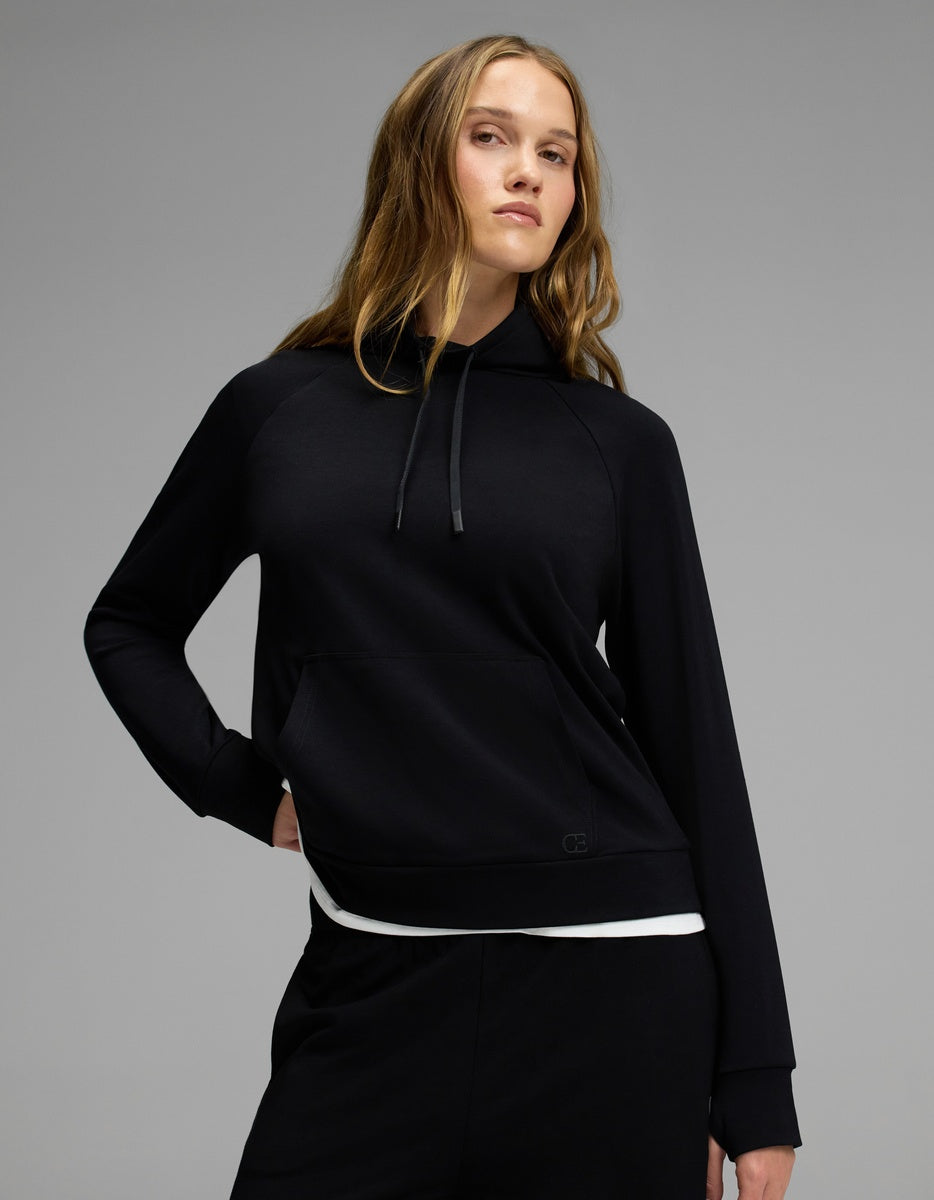 A person with long, wavy hair stands confidently against a plain gray background wearing Cozy Earth’s Women’s Brushed Bamboo Mock Neck in black and matching black pants.