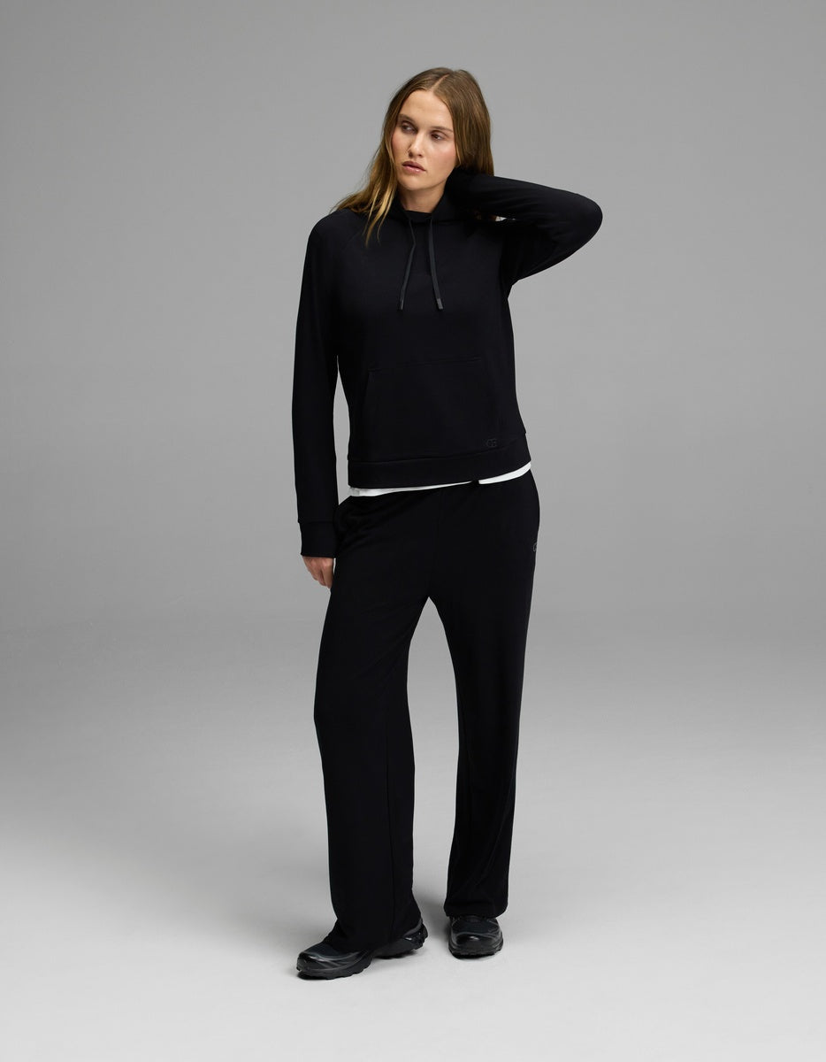 A woman stands in a relaxed pose, wearing the Cozy Earth Women’s Brushed Bamboo Mock Neck, paired with black pants and black shoes against a plain gray background.