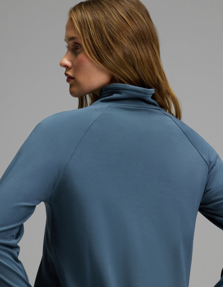 A woman with long brown hair wears the Cozy Earth Women’s Brushed Bamboo Mock Neck, shown from the back and in profile against a plain gray background.