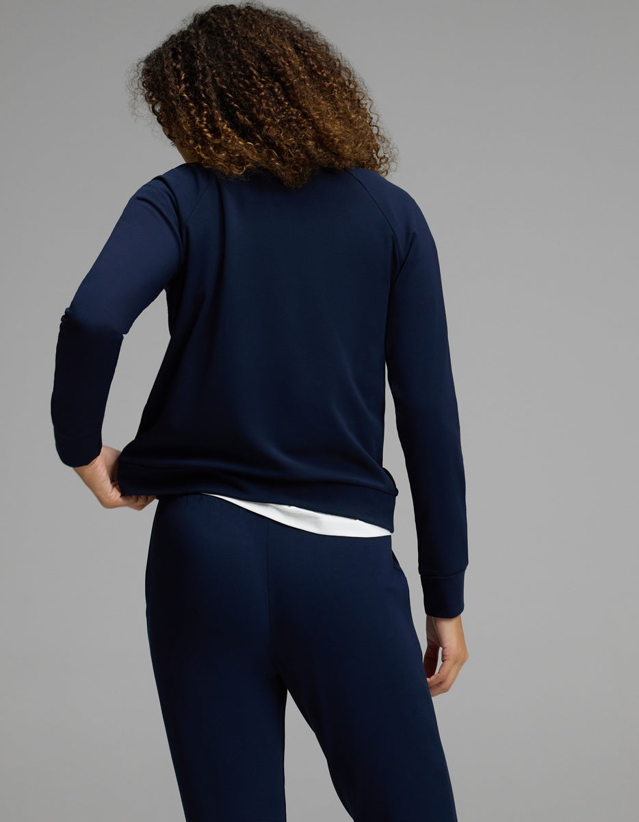 A person with curly hair, seen from behind, wears the Cozy Earth Women’s Brushed Bamboo Mock Neck & Jogger Set in navy over a white shirt, standing against a plain gray background.