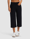 A person models the lower half of Cozy Earth's Women's Brushed Bamboo Pull On Capri in black with white sneakers, standing against a plain light background.|Color:Black
