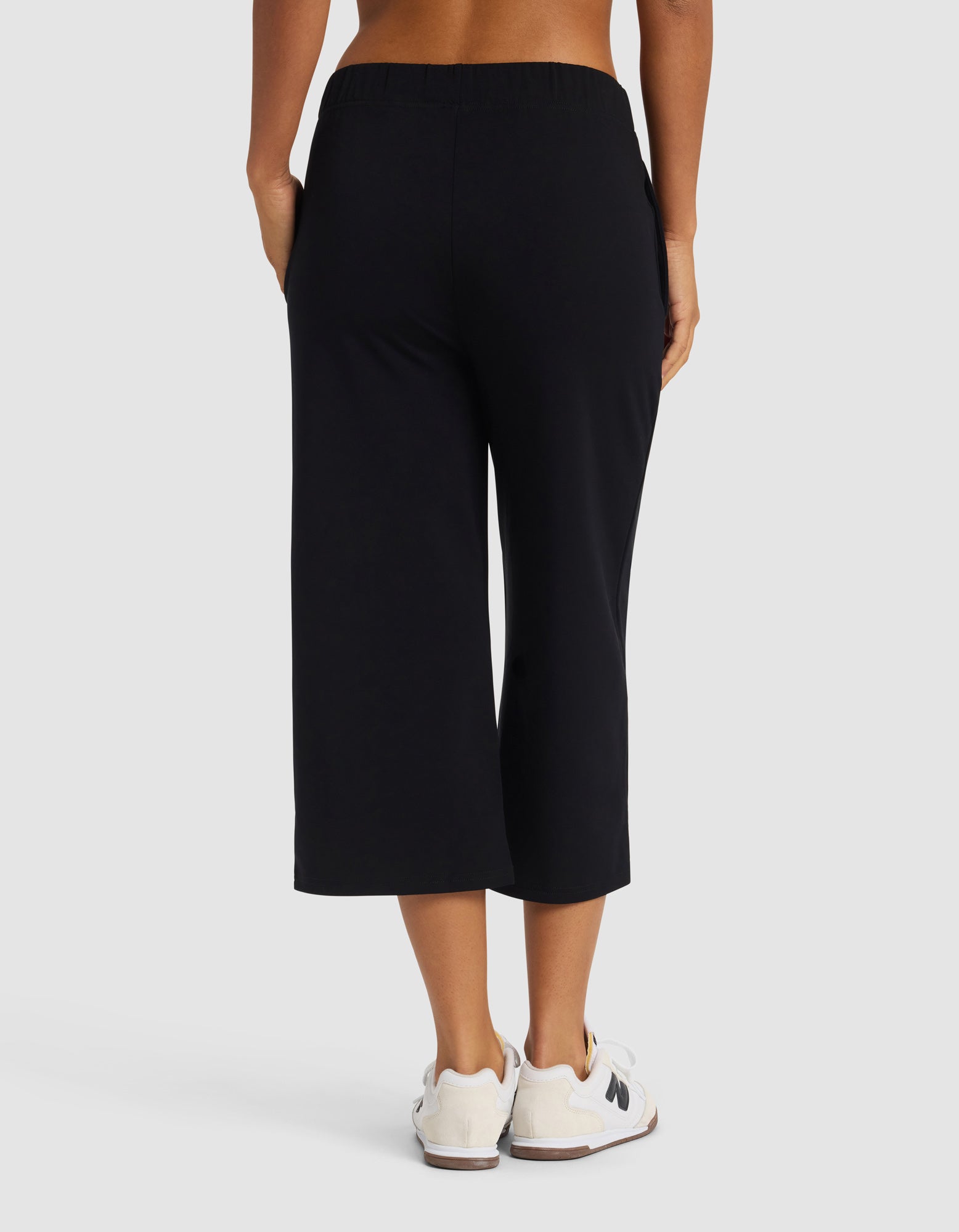A woman is shown from the waist down wearing Cozy Earth's Women's Brushed Bamboo Pull On Capri in black with white sneakers against a plain, light background.|Color:Black