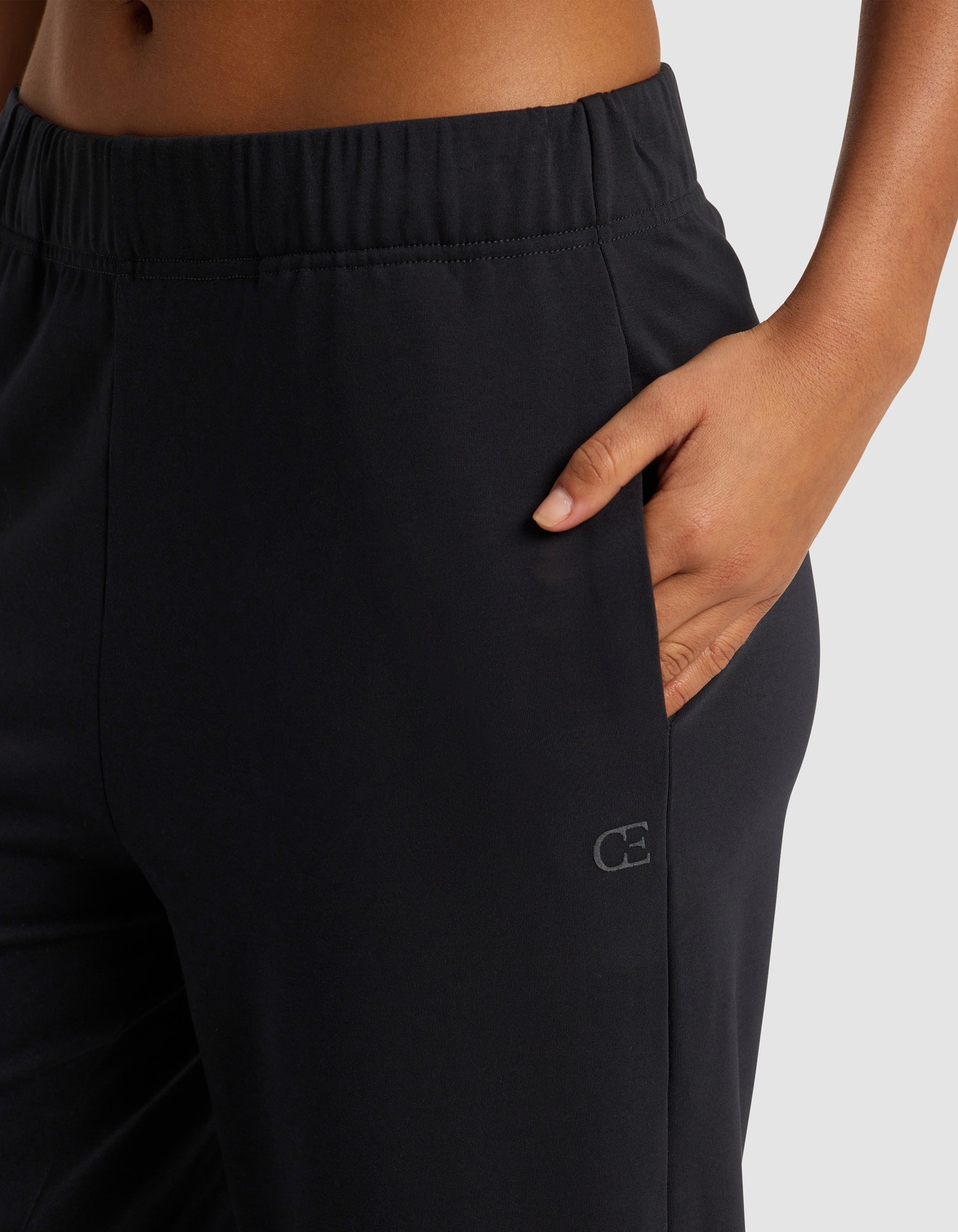 A person wears Cozy Earth's Women's Brushed Bamboo Pull On Capri in black, featuring an elastic waistband and a small logo near the pocket, with one hand in the right pocket against a light gray background.