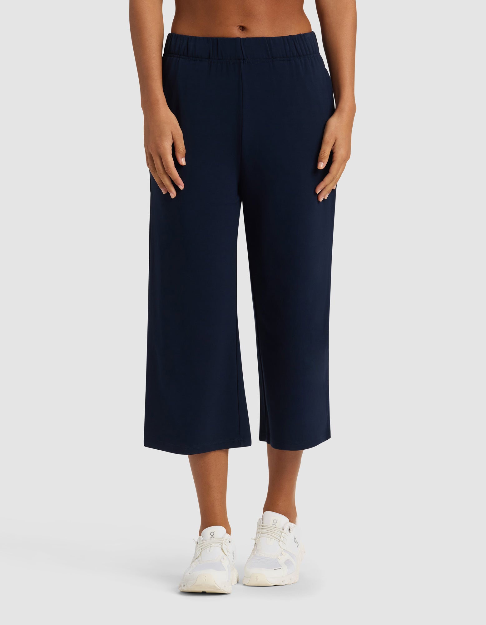 A person wearing Cozy Earth's Women's Brushed Bamboo Pull On Capri in navy blue with white sneakers and a bare midriff, standing against a plain light gray background.|Color:Navy