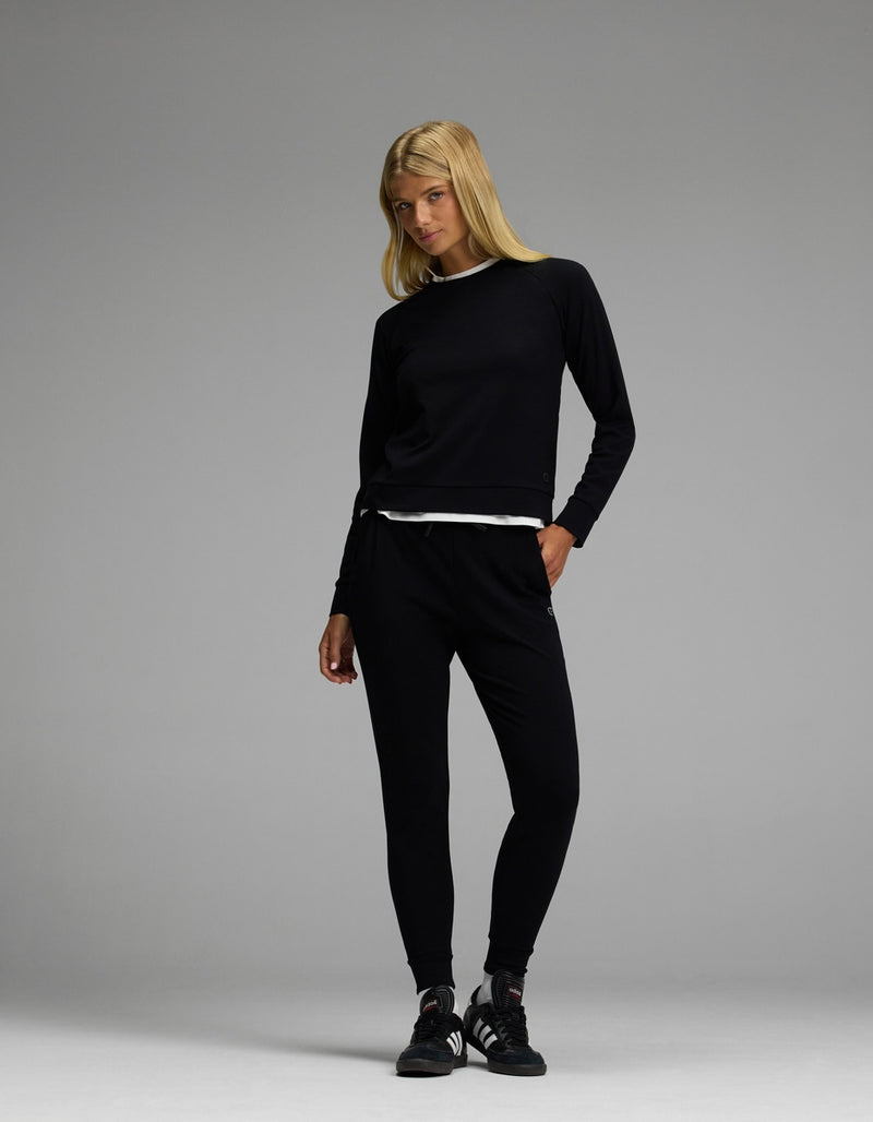 A woman with long blonde hair wears the Cozy Earth Women’s Brushed Bamboo Jogger Set in black, standing against a plain gray background.