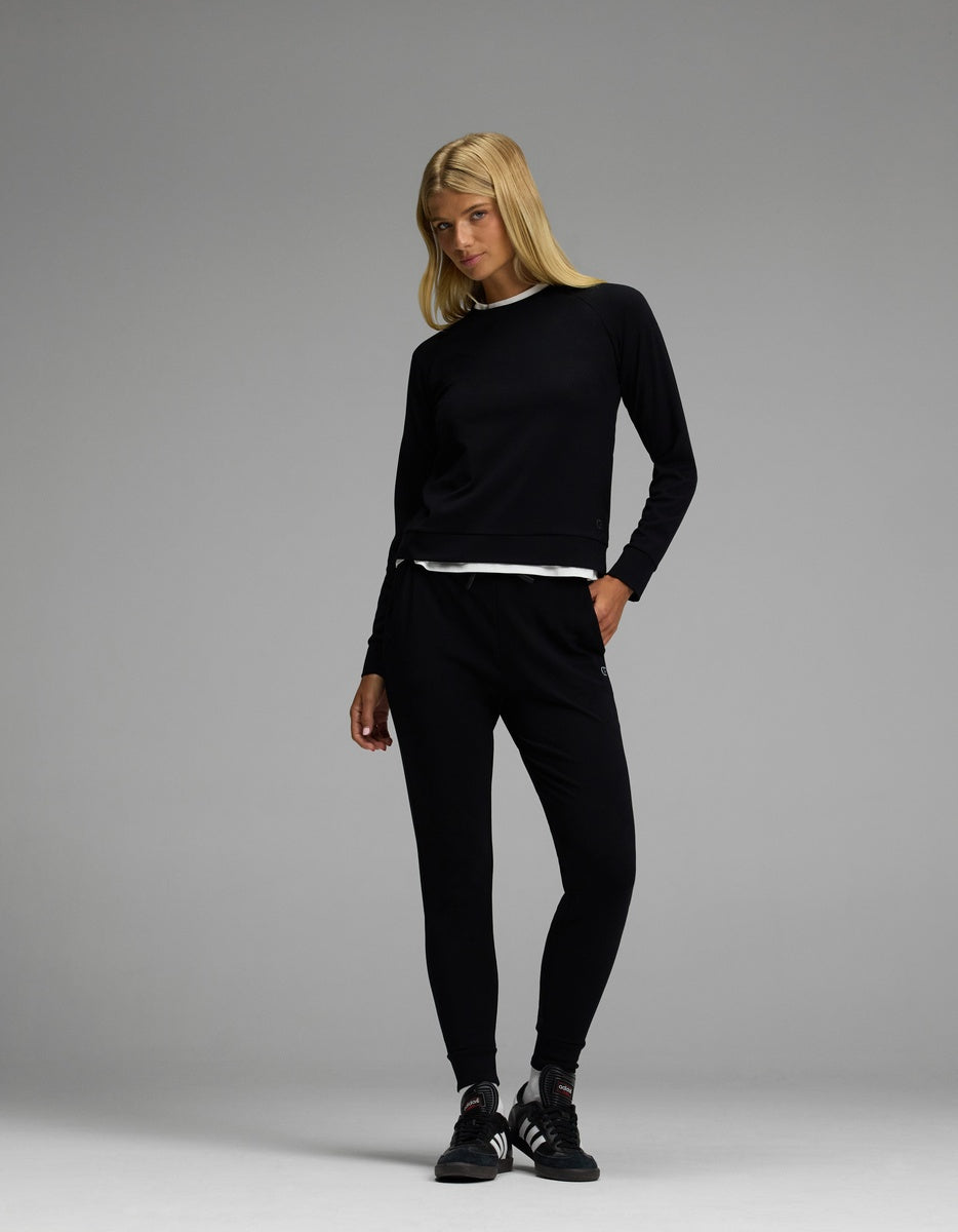 A woman with long blonde hair wears the Cozy Earth Women’s Brushed Bamboo Jogger Set in black, standing against a plain gray background.|Color:Black