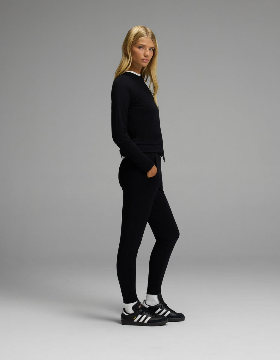 A woman with long blonde hair stands sideways against a plain gray background, wearing the Cozy Earth Women’s Brushed Bamboo Jogger Set in black.