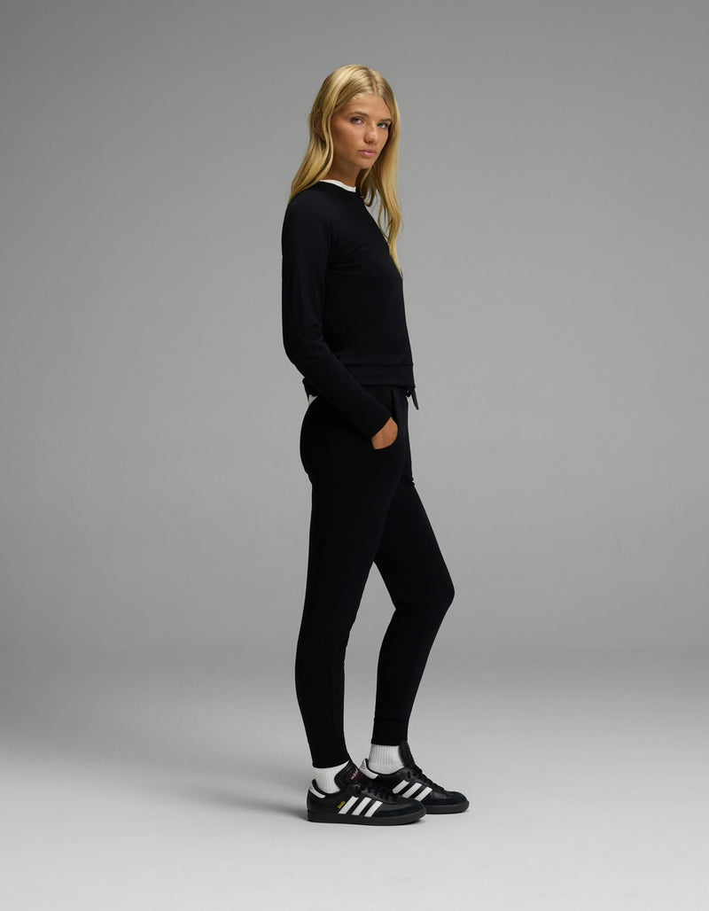 A woman with long blonde hair stands sideways against a plain gray background, wearing the Cozy Earth Women’s Brushed Bamboo Jogger Set in black.
