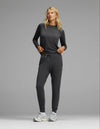 A woman with blonde hair stands against a gray background wearing the Cozy Earth Women’s Brushed Bamboo Jogger Set in Charcoal, paired with white sneakers. Her hands are in her pockets.|Color:Charcoal