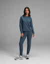 A woman stands against a plain gray background wearing the Cozy Earth Women’s Brushed Bamboo Jogger Set in Dawn with gray sneakers, looking at the camera with a neutral expression.|Color:Dawn